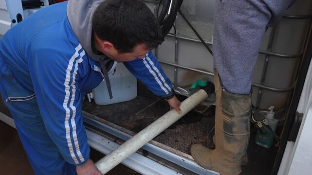Farmer crouches inside a van holding a pipe to empty the water tank used for agricultural drone operations