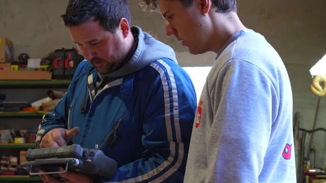 Close up of young and adult farmers jointly operating a drone controller inside a barn environment