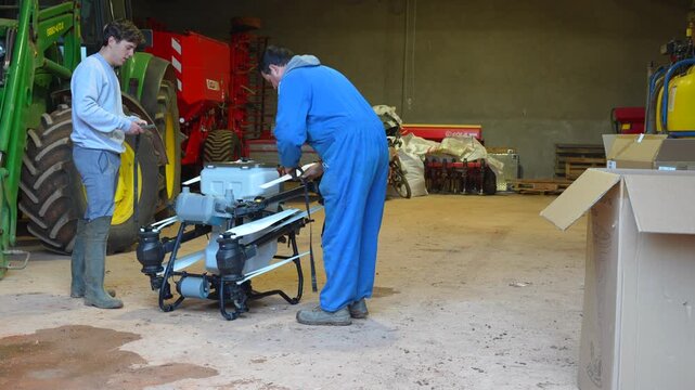 Farmers inside a barn secure folded drone propellers with elastic bands to prepare safe transport before field work