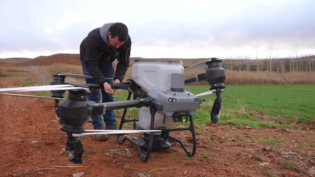 Farmer secures agricultural drone arms with cable ties before operating it with a solids tank in a wheat field