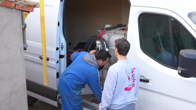 Young and adult farmers manage a pipe near a water tank inside a van during agricultural preparation work