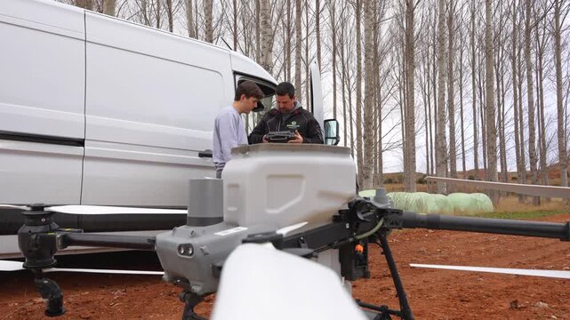 Static view from drone propeller shows two farmers configuring the remote controller before agricultural drone takeoff in the field