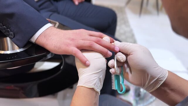 Professional manicure close-up: gloved technician trims cuticles and preps nails on male client hands in modern spa salon. Hygienic beauty treatment and grooming.