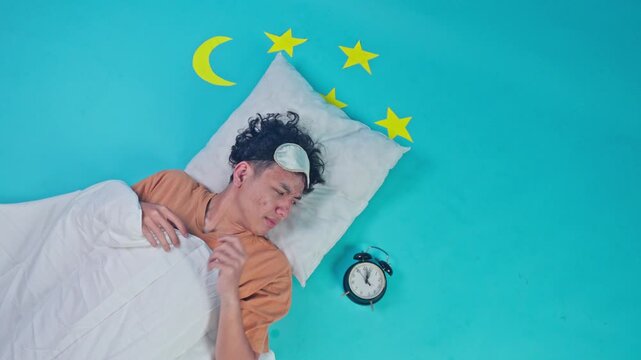 High angle shot of sleepy man turning off alarm clock while lying on pillow in studio
