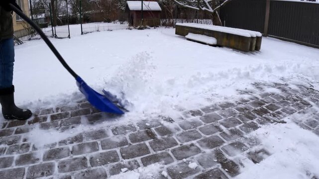 Person shoveling snow from a brick path in a winter backyard scene
