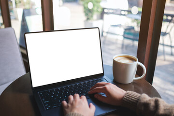 Fototapeta premium Mockup image of a woman working and typing on laptop computer with blank white desktop screen in cafe