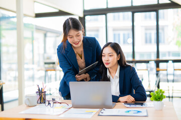 Obraz premium Group of happy Asian business people having a meeting at the office. Two women working together using modern laptops.