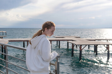 Fototapeta premium A teenage girl walks along the beach and pier at sunset on Lake Issyk-Kul. Concept: Family vacation trip
