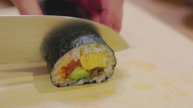 Close-up of hands cutting futomaki sushi roll with a kitchen knife