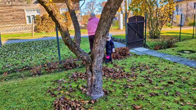 Parents and children working together, raking fallen autumn leaves in a green garden