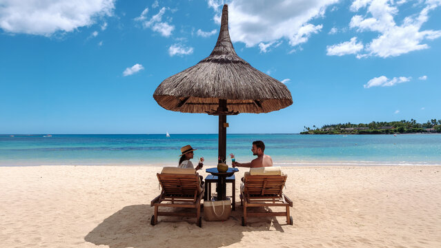 Relaxing together on a beautiful beach in Mauritius with drinks under a thatched umbrella