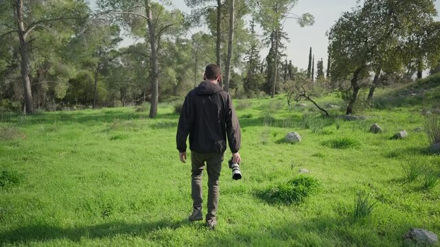 Videographer walking slowly through green forest while holding camera during outdoor shoot.