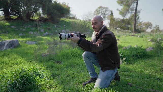 Camera operator kneeling in a green forest while filming a low angle shot with a professional mirrorless camera.