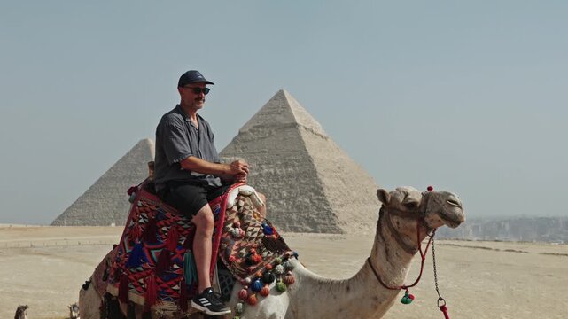 Classic Egyptian travel experience: a man sitting atop a camel at the Giza Plateau. The camel is adorned with a vibrant, traditionally patterned saddle.