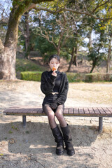 Obraz premium Young woman smiles softly, leaning against tree trunk. Black knit top and sparkly cardigan add stylish contrast. Dark shorts and sheer tights complete her trendy look