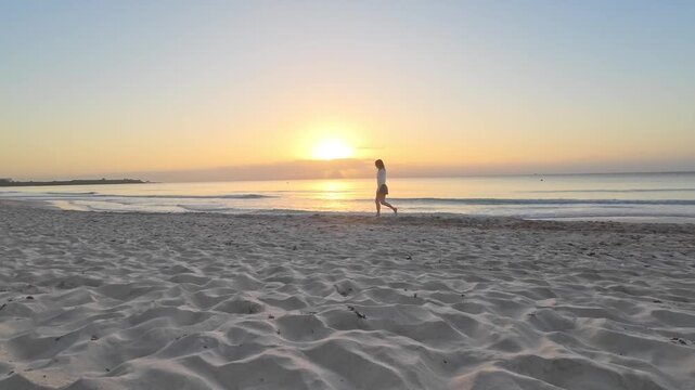 Woman walking at sunrise sunset golden hour on a calm peaceful Tulum beach. Mindfulness, wellness, and tropical relaxation.