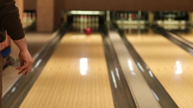 Man in brown clothing releases a red bowling ball down the lane, capturing the motion of the throw in a vibrant bowling alley setting