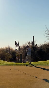Golfer almost makes chip shot at sunset on Arizona desert course, with large cactus backdrop, vertical 4k sunny day