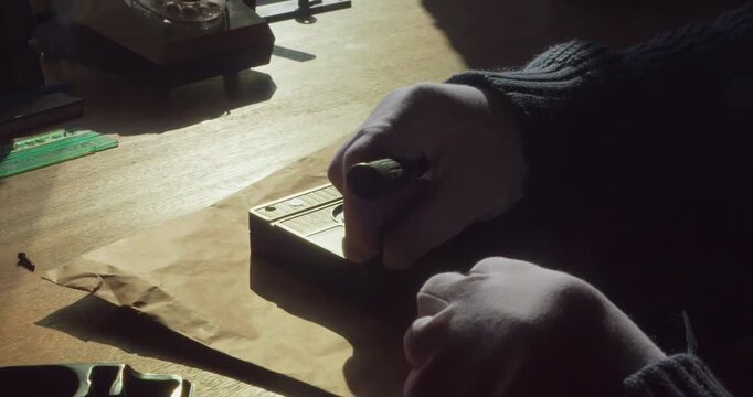 Close-up of a white-gloved technician removing the back casing of an analog VHS tape to access the internal components.