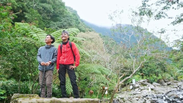 Two hikers standing stream pointing at scenic view on rock by mountain