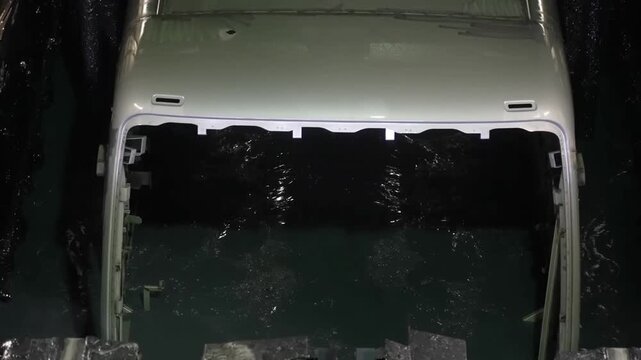 Large bus chassis being submerged into an industrial E-coat dip tank for anti-corrosion treatment