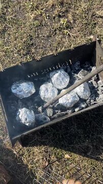 A man turns over coals and foil-wrapped potatoes for grilling on a barbecue