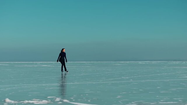 Drone shot capturing a woman ice skating across a vast frozen lake as the camera gradually moves closer