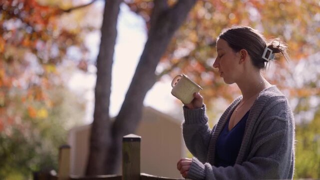 A woman admiring the fall foliage in her backyard while drinking a cup of coffee