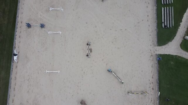 A Birds eye view from a drone of an outdoor Equestrian arena and a Horseback rider trotting along the course.