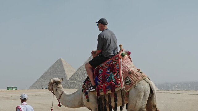 Classic Egyptian travel experience: a man sitting atop a camel at the Giza Plateau. The camel is adorned with a vibrant, traditionally patterned saddle.