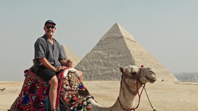 Classic Egyptian travel experience: a man sitting atop a camel at the Giza Plateau. The camel is adorned with a vibrant, traditionally patterned saddle.