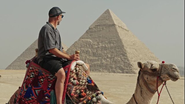 Classic Egyptian travel experience: a man sitting atop a camel at the Giza Plateau. The camel is adorned with a vibrant, traditionally patterned saddle.
