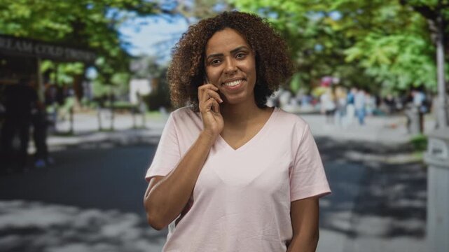 Woman talking on smartphone on a busy street, smiling with hand to ear and visible face; happy conversation.