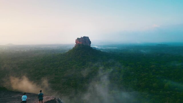 Cinematic aerial video of man and woman walking on Pidurangala mountain and looking to Lions Rock in Sigiriya.