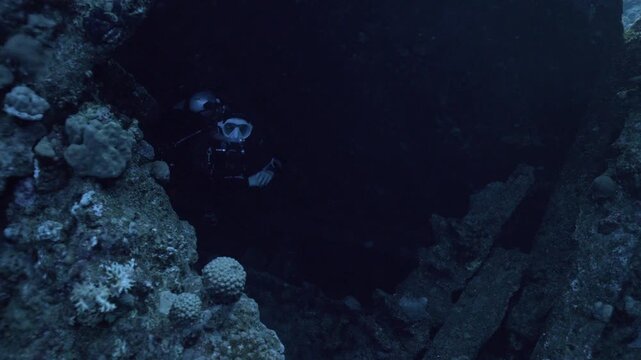 A scuba diver emerges from the shadowy, interior of the Giannis D wreck, transitioning through a section of the superstructure into the exterior waters of Abu Nuhas