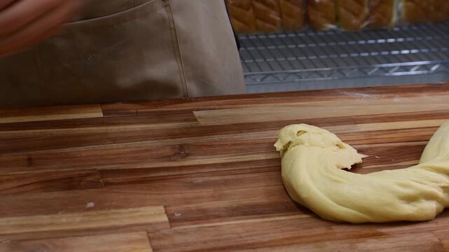 Close-up of a baker hands using a dough scraper to cut dough and roll it into balls on a wooden kitchen table, showing artisanal bread-making technique.