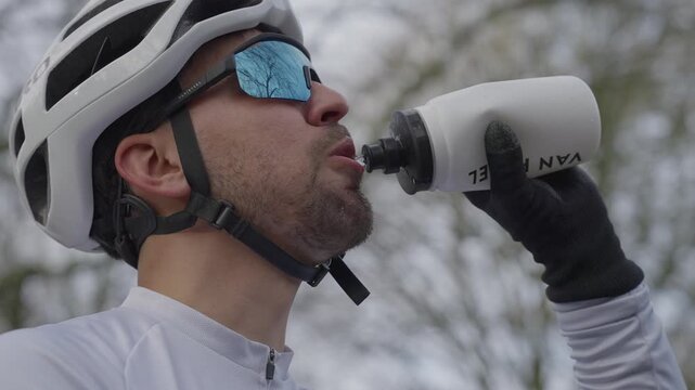 Man wearing helmet and sunglasses drinking from sports bottle while cycling