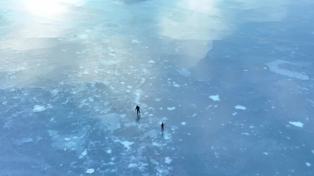 Static aerial view of father and daughter skating on frozen lake in calm winter light