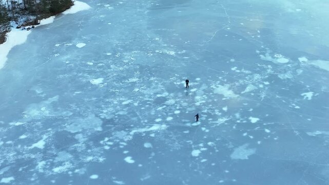 Aerial orbit shows father and daughter skating on frozen lake surrounded by winter ice