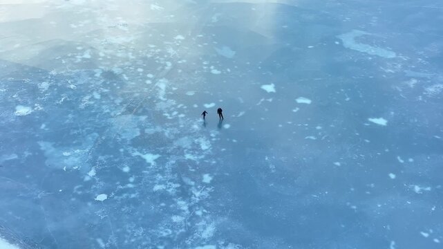 Aerial view of father and daughter skating together diagonally on frozen lake in winter