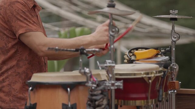 Percussionist performing on bongos with cymbals in outdoor setting