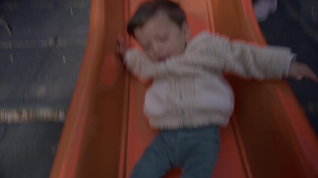Lifestyle clip of a grandmother gently holding a young child at the top of a playground slide in a forest park, then letting go as the child slides down while the camera follows the movement, capturin