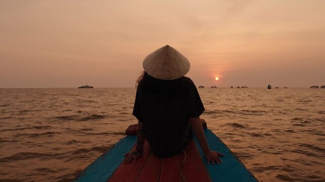 Person watching a warm sunset on Tonle Sap Lake while sitting on a boat.