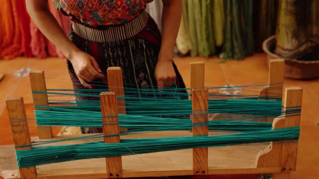 Artisan winds dyed thread onto a wooden loom for textile weaving