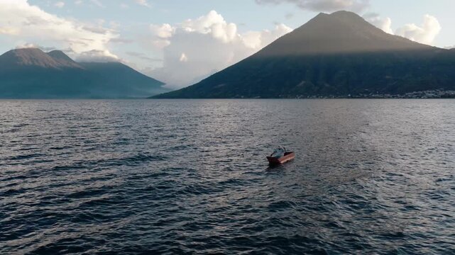 A lone canoe crosses Lake Atitlan framed by volcanic mountains in Guatemala
