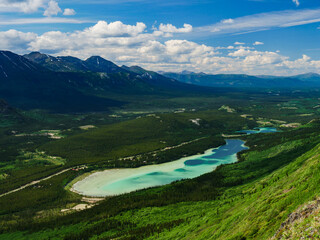 Fototapeta premium Majestic mountain vista with a serene turquoise lake reflecting the vast expanse of the blue sky and scattered clouds