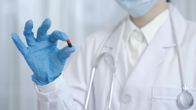 A faceless doctor pharmacist in white uniform with stethoscope holding a vibrant red and black capsule pill vitamin. Receiving vitamins or medications. Medical, pharmacy and healthcare concept