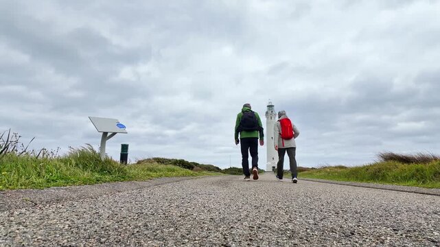 a mature couple in trekking outfits walking past low lying camera along a footpath towards Cape Leeuwin Lighthouse.