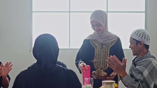 Muslim family smiling and applauding as woman serves ketupat during festive Lebaran lunch at home
