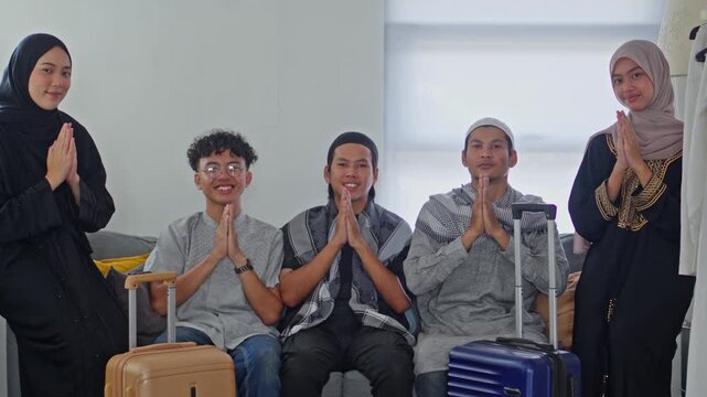 Muslim family in traditional clothes with suitcases smiling and giving greeting gestures